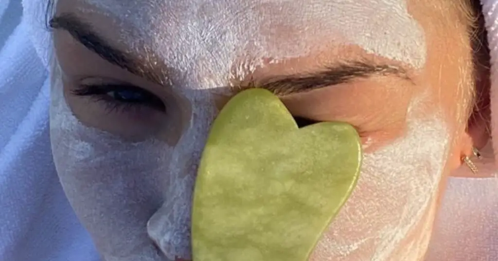woman holding jade gua sha infront of her face