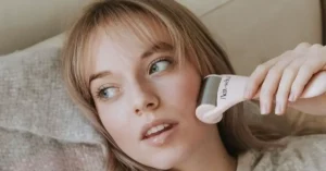 young blonde woman using ice roller on her left cheek
